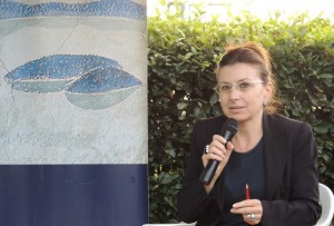 Stefania Limiti presenta il suo lavoro accanto al poster stilizzato di Isola Maggiore, Isola del Libro.