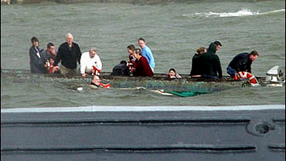 I passeggeri sopravviventi si rifugiano sullo scafo della barca-pontone rovesciata mentre una nave della US Navy arriva al loro soccorso.<br />  AP/US NAVY, Jerry Neblett.